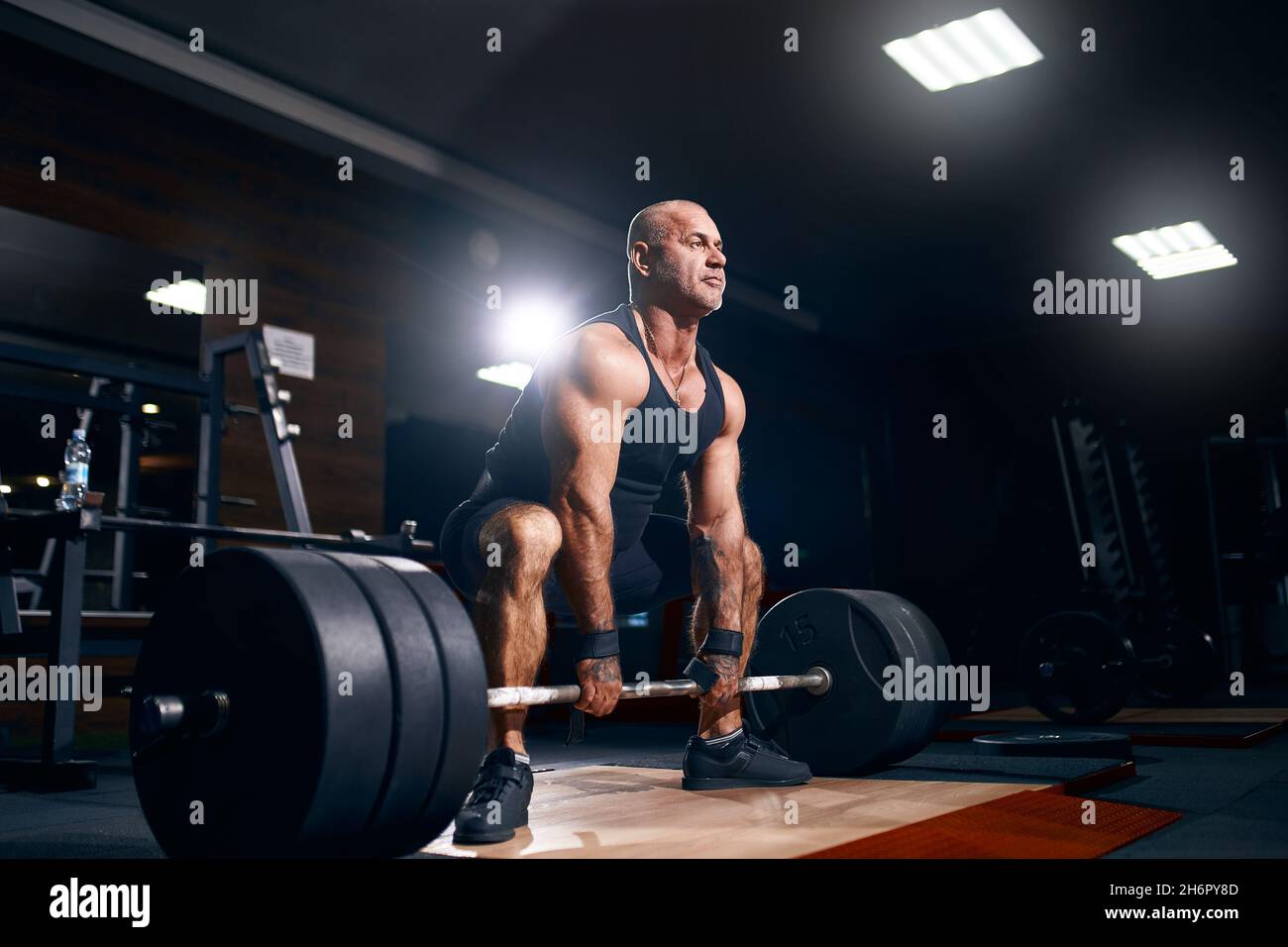 Adult bald powerlifter bodybuilder exercising deadlift barbell in gym