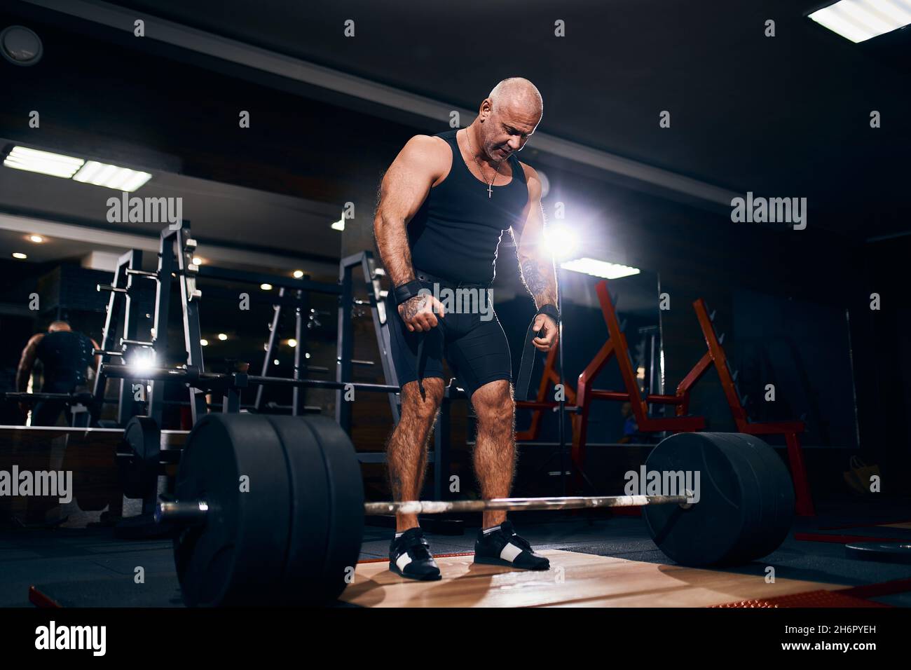 Adult bald powerlifter bodybuilder preparing deadlift barbell in gym