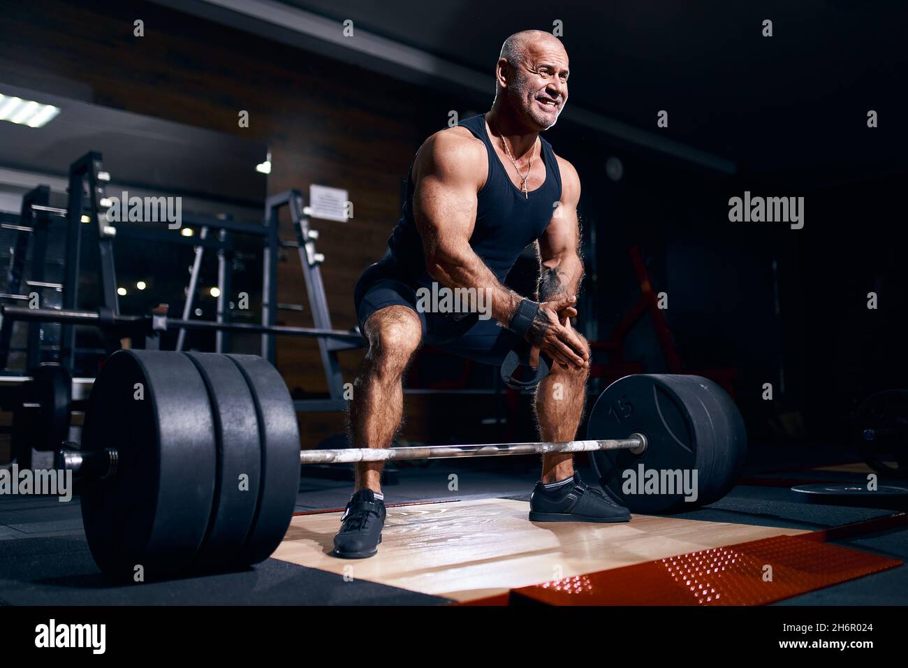 Adult bald man powerlifter bodybuilder preparing deadlift barbell in