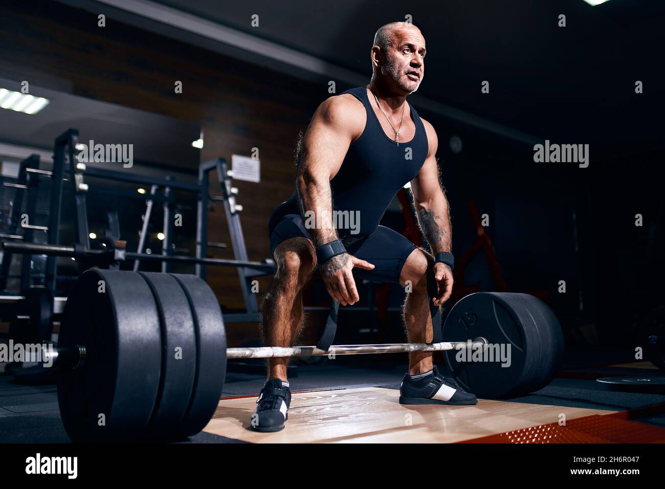 Adult bald male powerlifter bodybuilder preparing deadlift barbell in