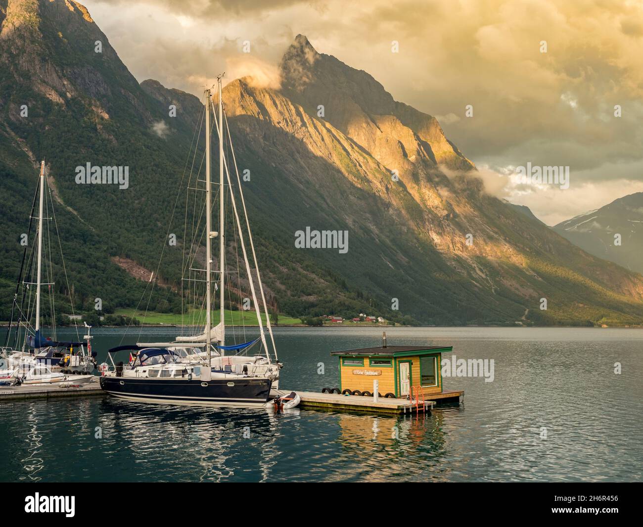 Boats and floating sauna, marina of village Urke at the Hjorundfjord, mt. Slogen in the back, sunset, Norway Stock Photo