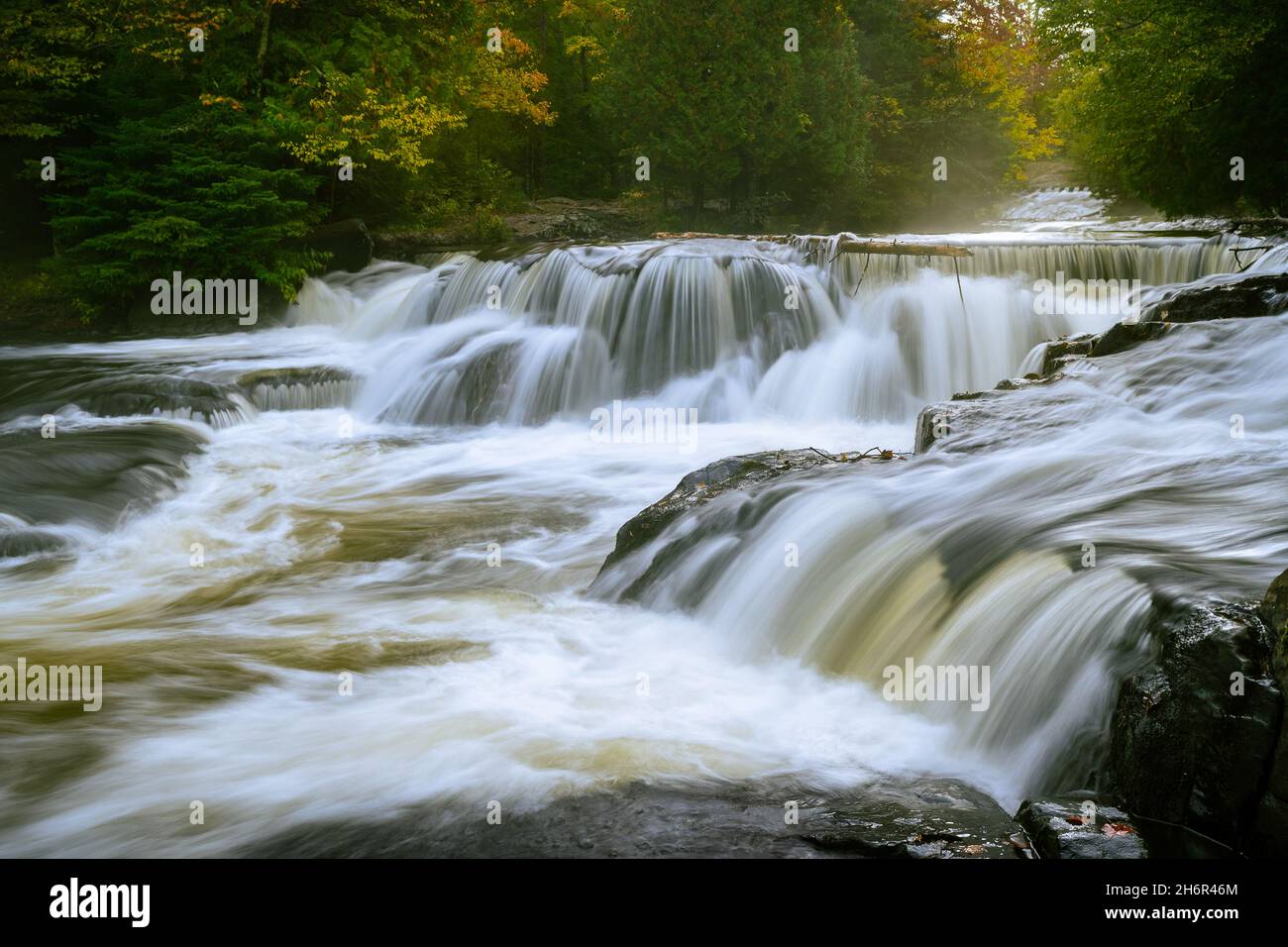 Long exposure of moving stream of water of the waterfalls at Bond Falls (Upper Falls) near Paulding, Michigan during autumn at sunrise Stock Photo