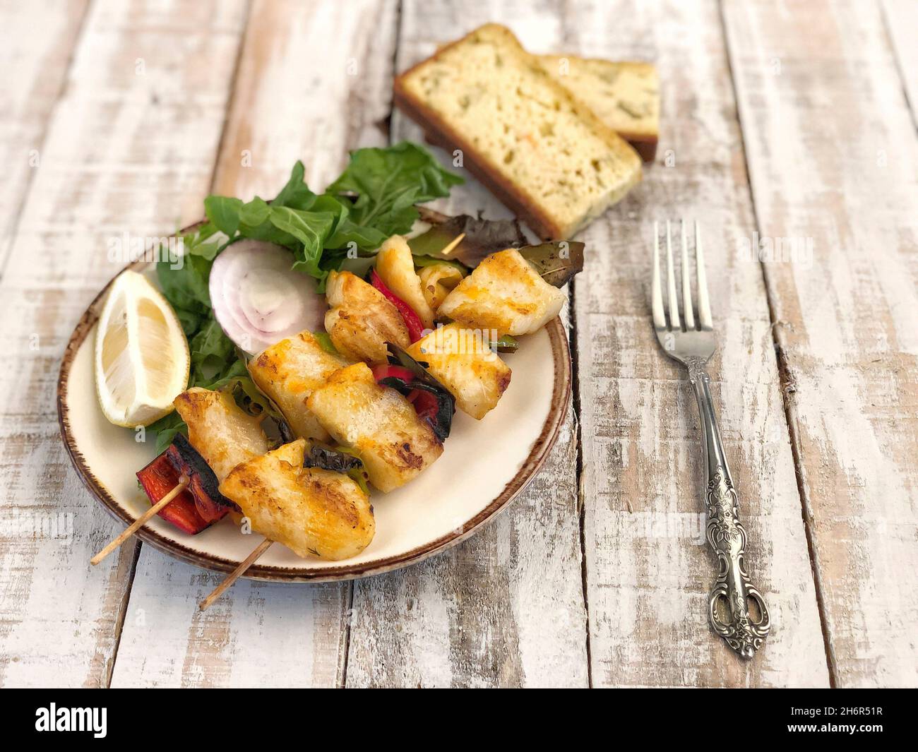 Skewed sole fish served with salad and sliced corn bread on table Stock Photo