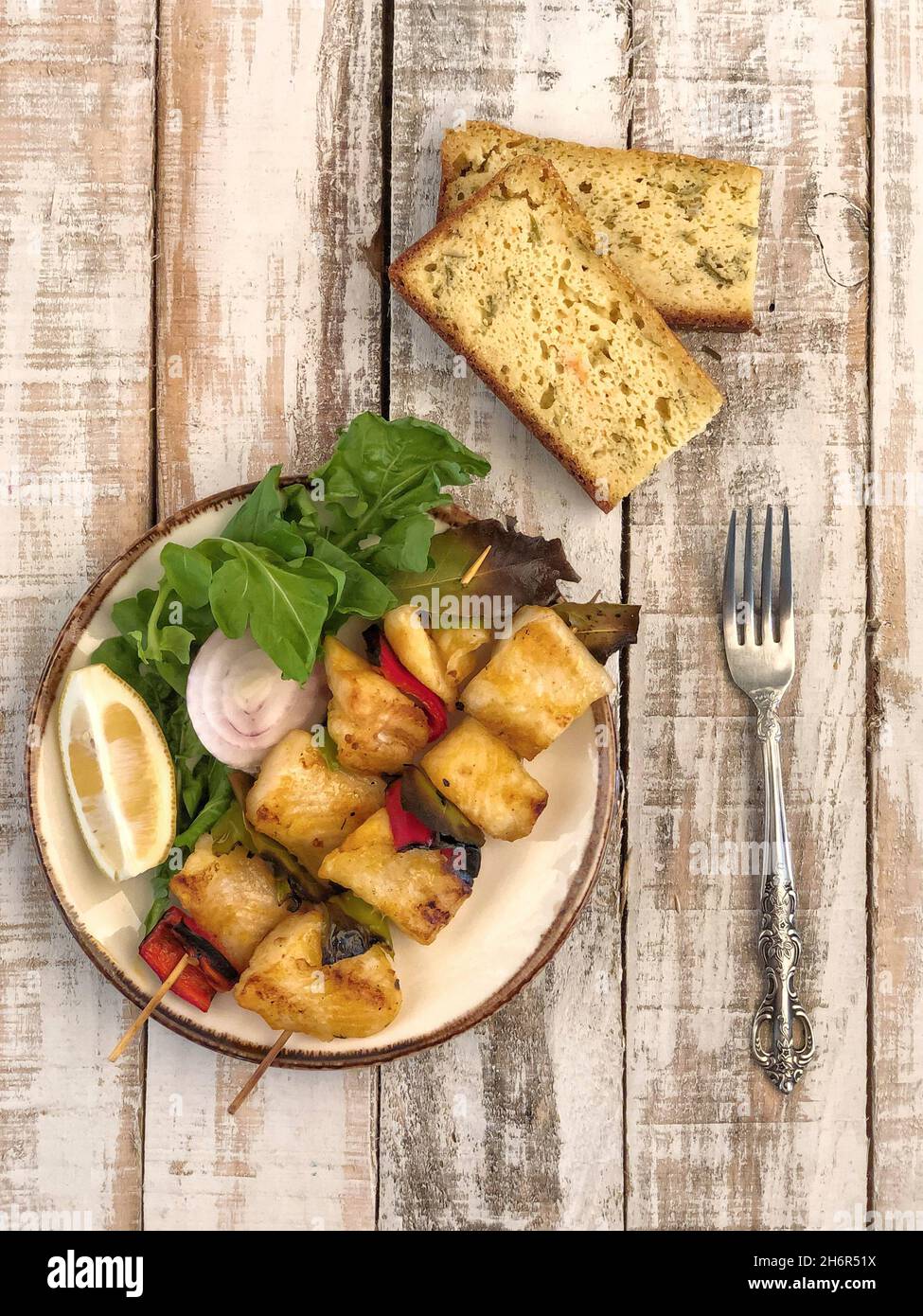 Skewed sole fish served with salad and sliced corn bread on table Stock Photo