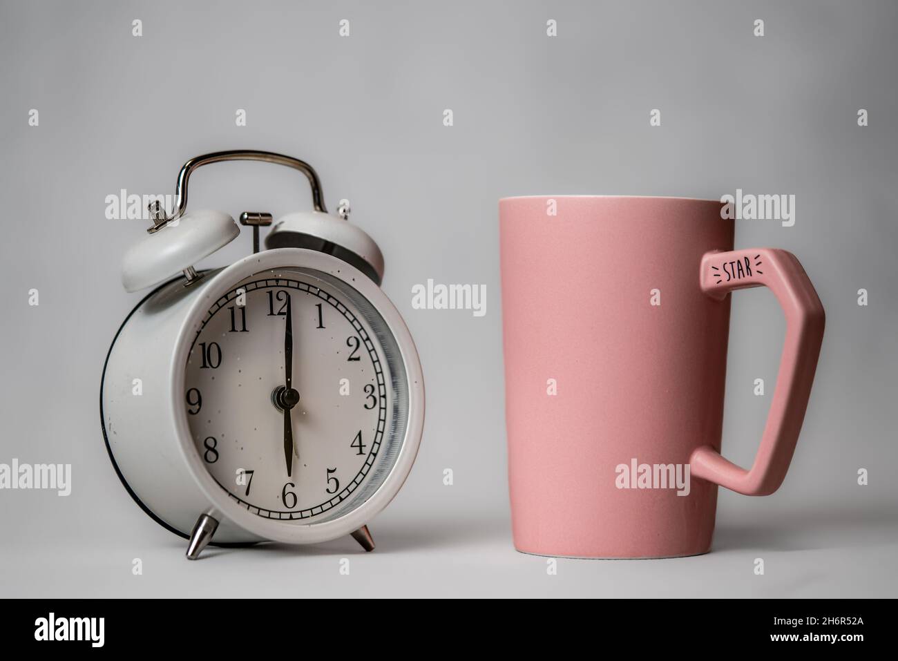 A black alarm clock in retro style and a rose coffee cup on a small saucer stand on a background. Good morning concept. Morning coffee Stock Photo