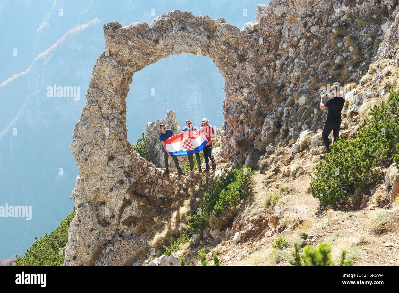 People holding flag of Croatia in natural arch 'Hajdučka vrata' in Blidinje natur park (Jablanica, Bosnia and Herzegovina) Stock Photo