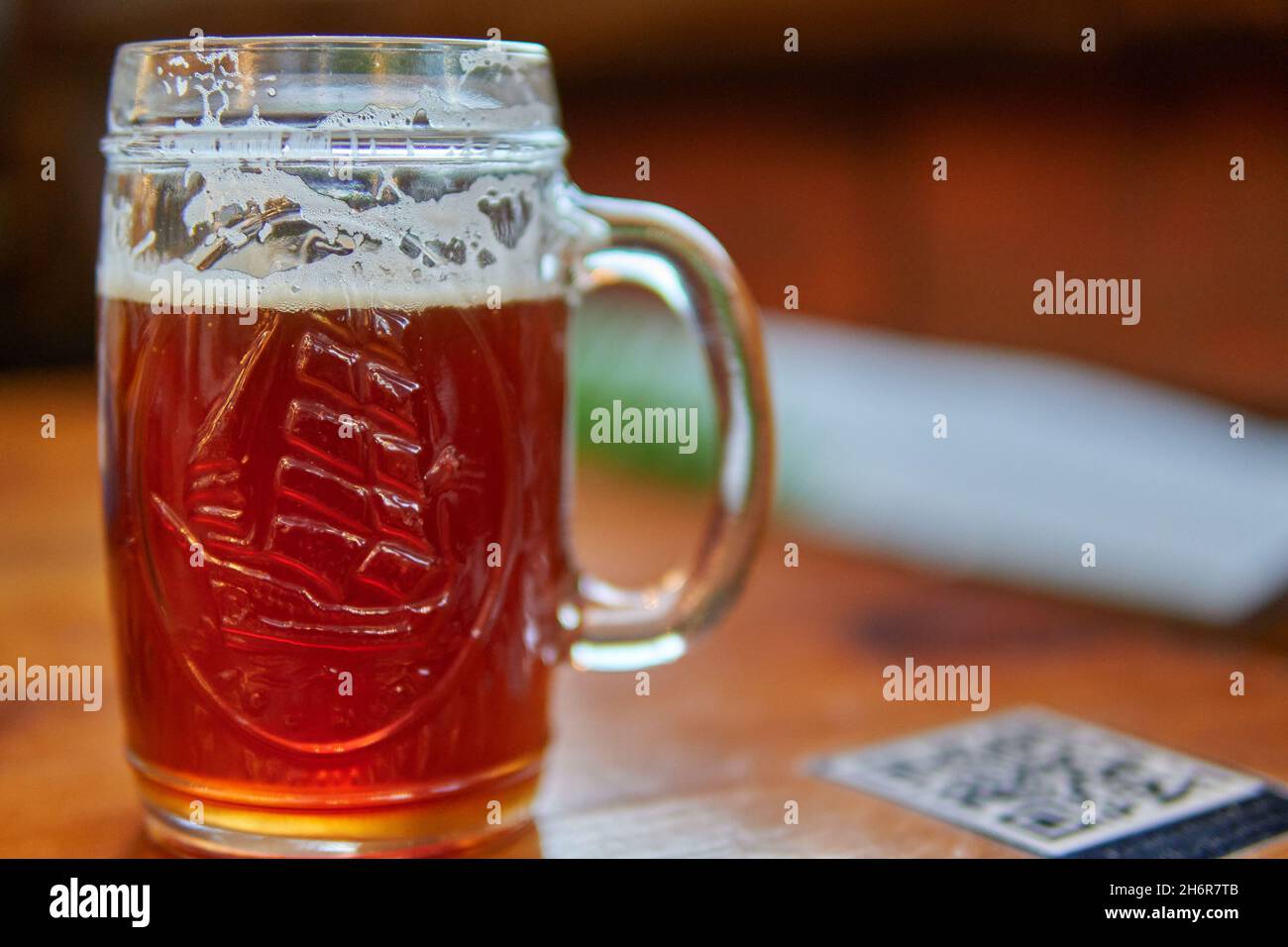 Pint of craft beer mug on a table with a blurred qr code stuck on the table to see the pub menu with mobile phone. New normality after covid. Horizont Stock Photo