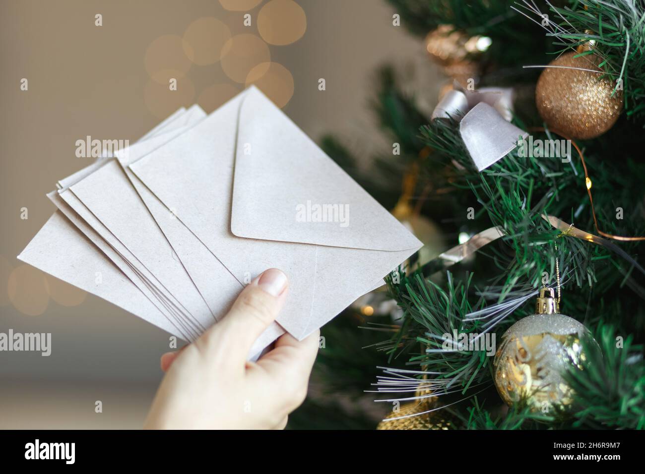 https://c8.alamy.com/comp/2H6R9M7/hand-holding-stack-of-craft-paper-envelopes-for-christmas-greeting-card-invitation-design-on-christmas-tree-background-with-bokeh-2H6R9M7.jpg