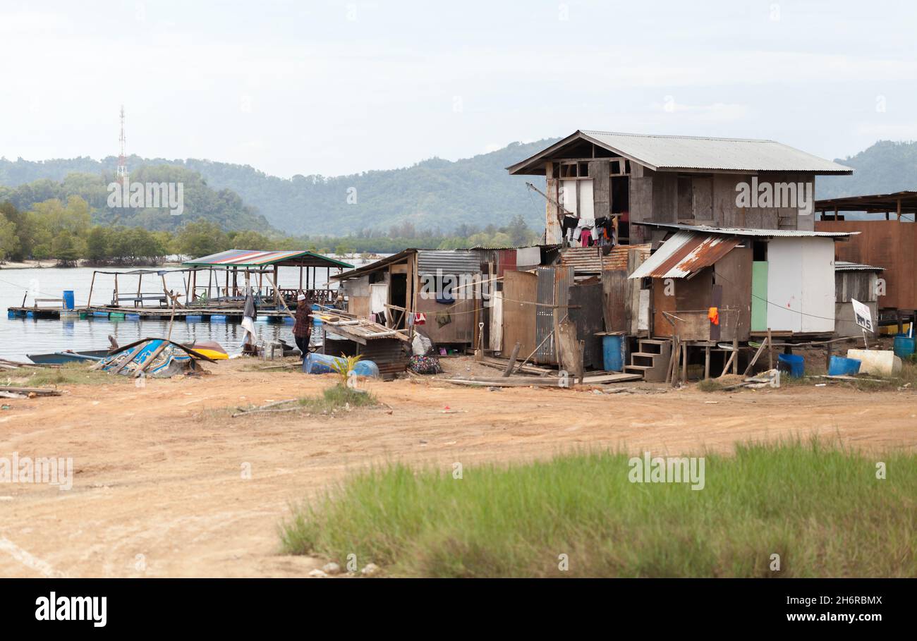 Tuaran, Malaysia - March 23, 2019: Poor wooden houses on the coast of Mengkabong River, local man walk nearby Stock Photo