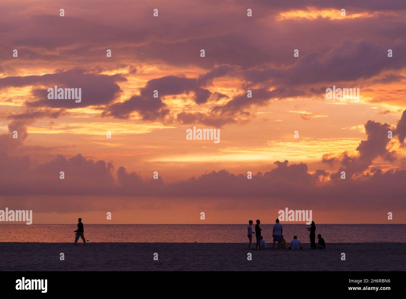 Kota Kinabalu, Malaysia - March 22, 2019: Tourists walk the Dalit Beach of Sabah under colorful sunset sky Stock Photo