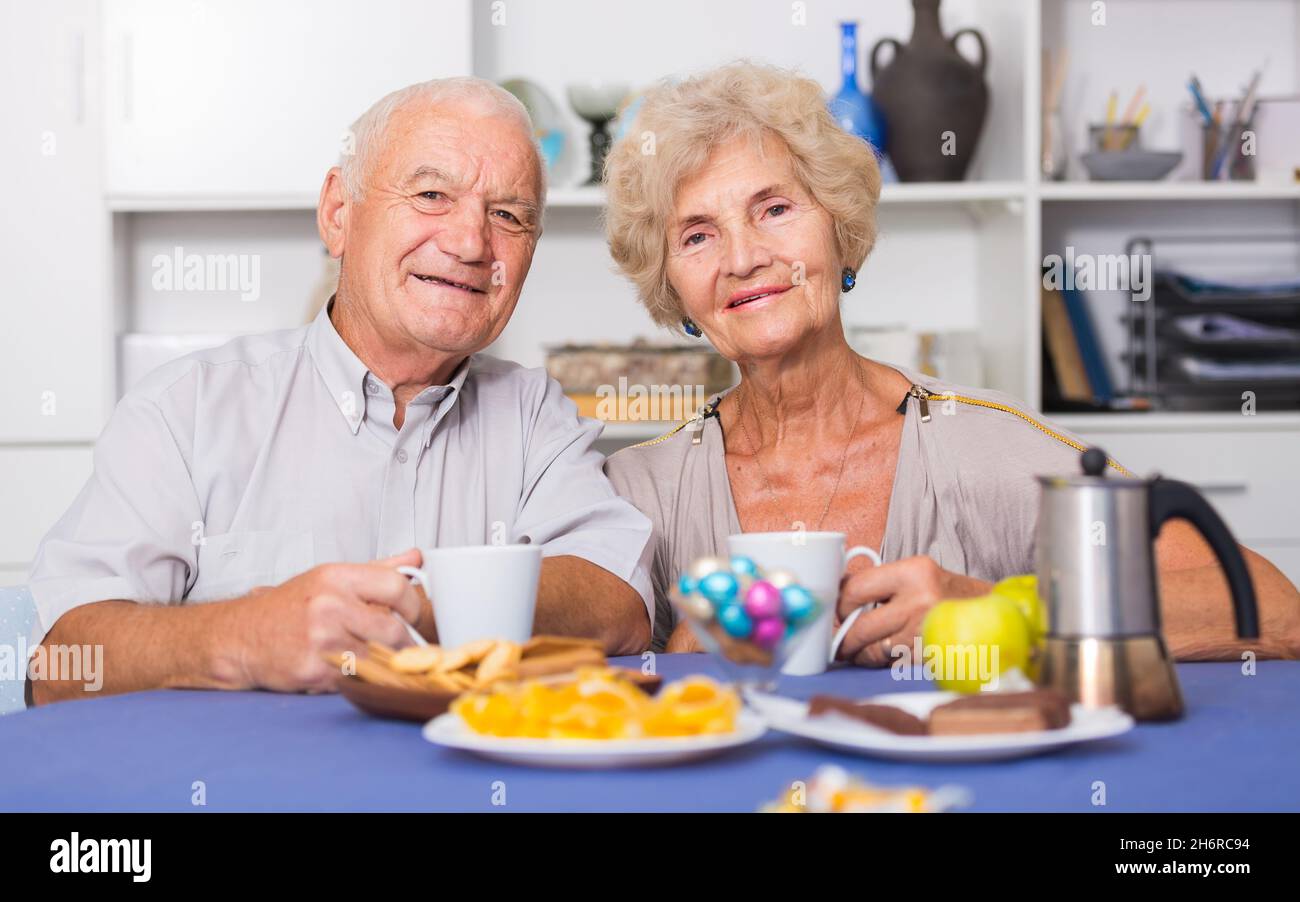 Smiling elderly spouses enjoying tea with sweets Stock Photo