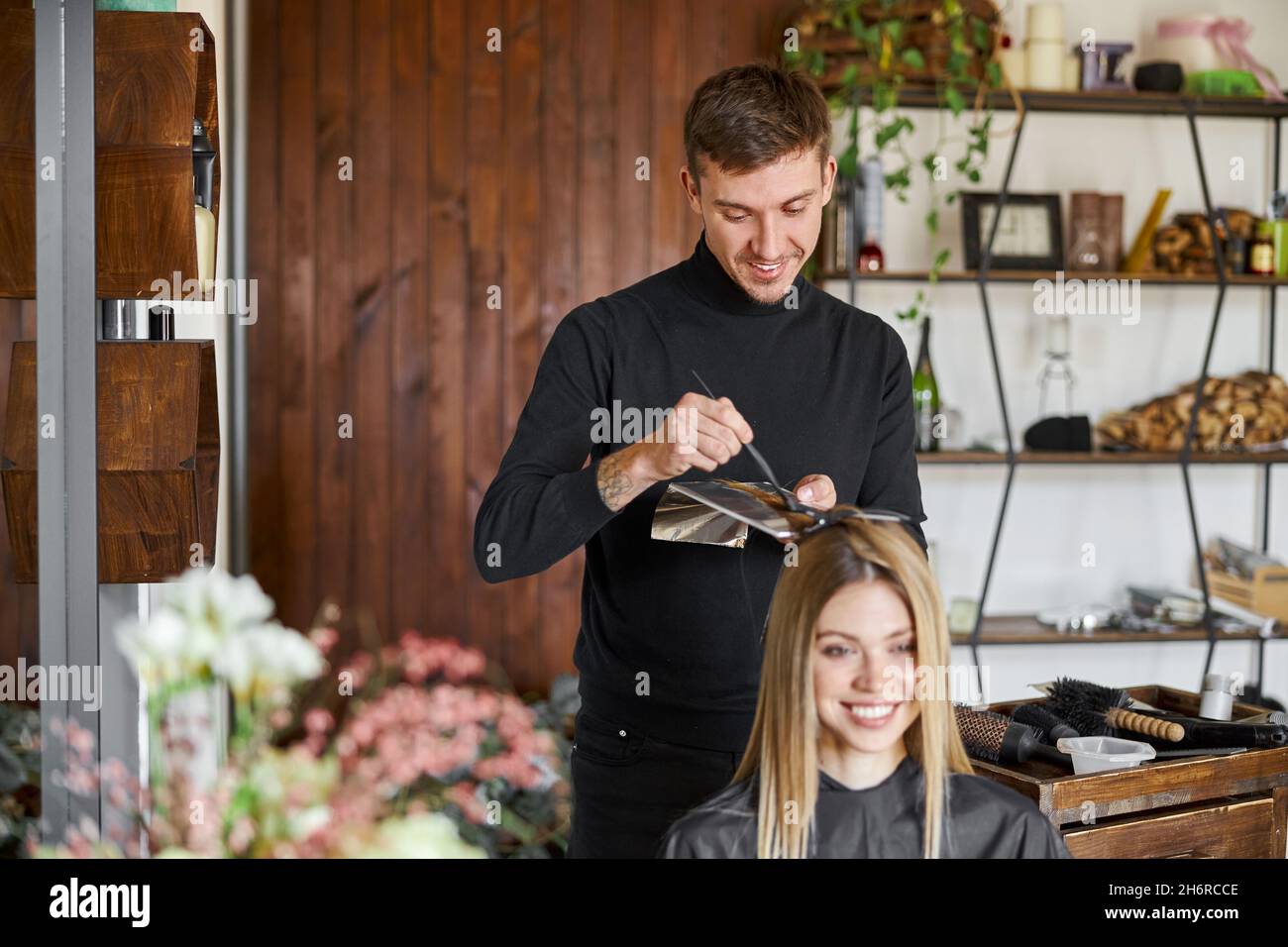 Confident male stylist is dyeing hair of blond caucasian female client ...