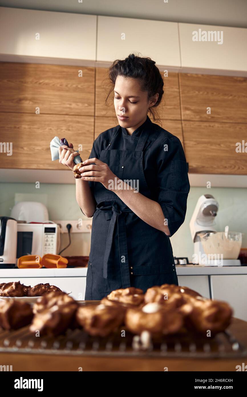 young professional female cook is preparing tasty cake at her light modern kitchen Stock Photo