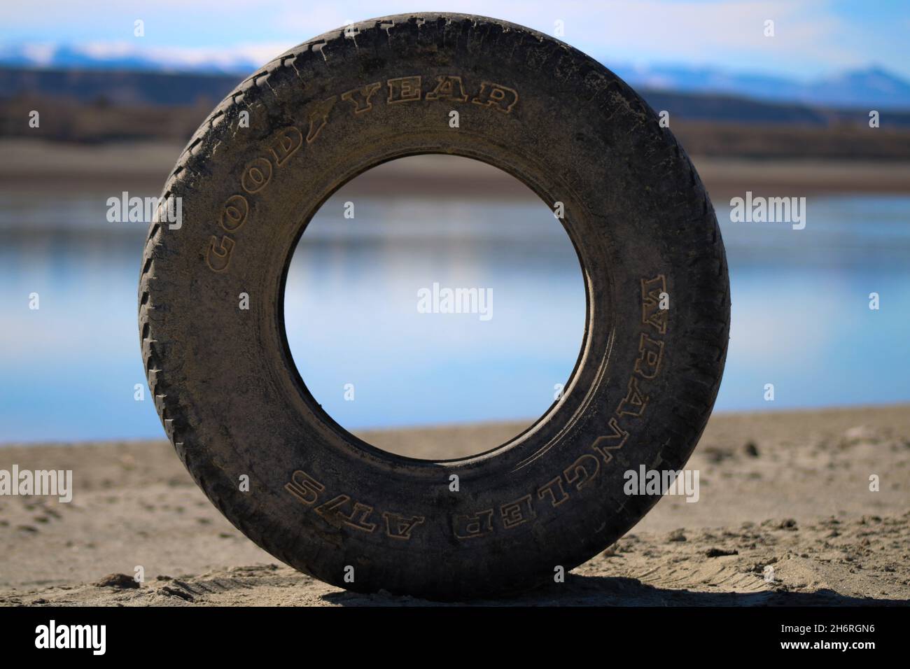 Rouged Goodyear tire lake beach in background environment trash Stock Photo