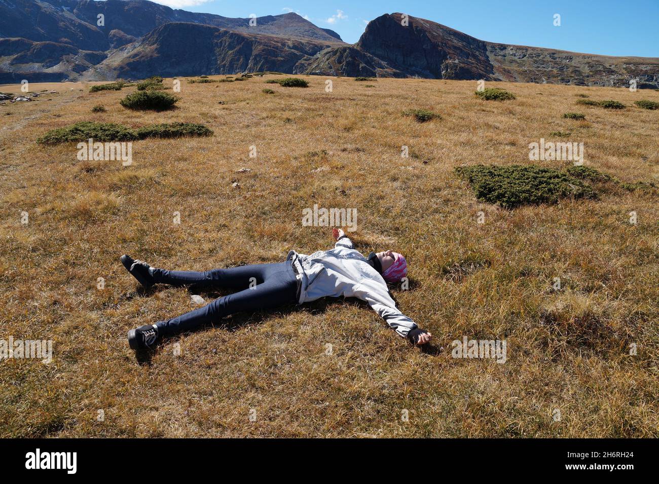 resting teenage girl lying on the ground with outstretched arms on a plateau in the mountains, halt Stock Photo
