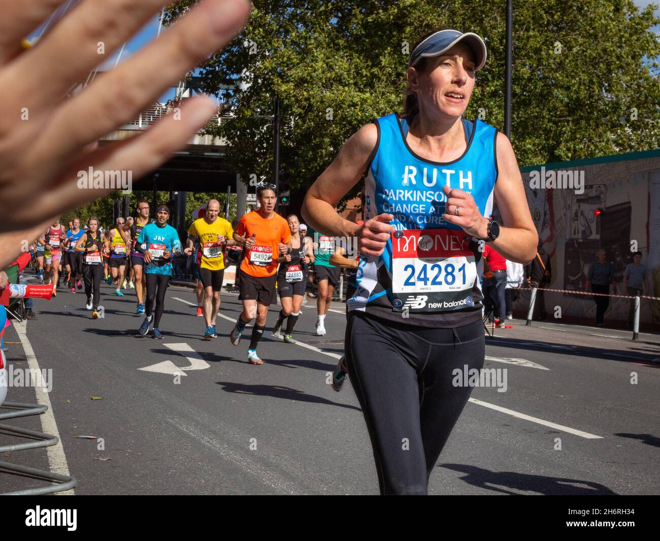 Woman running with spectator's hand in foreground, Virgin Money London Marathon 2021 at the 25 mile point, Victoria Embankment. Stock Photo