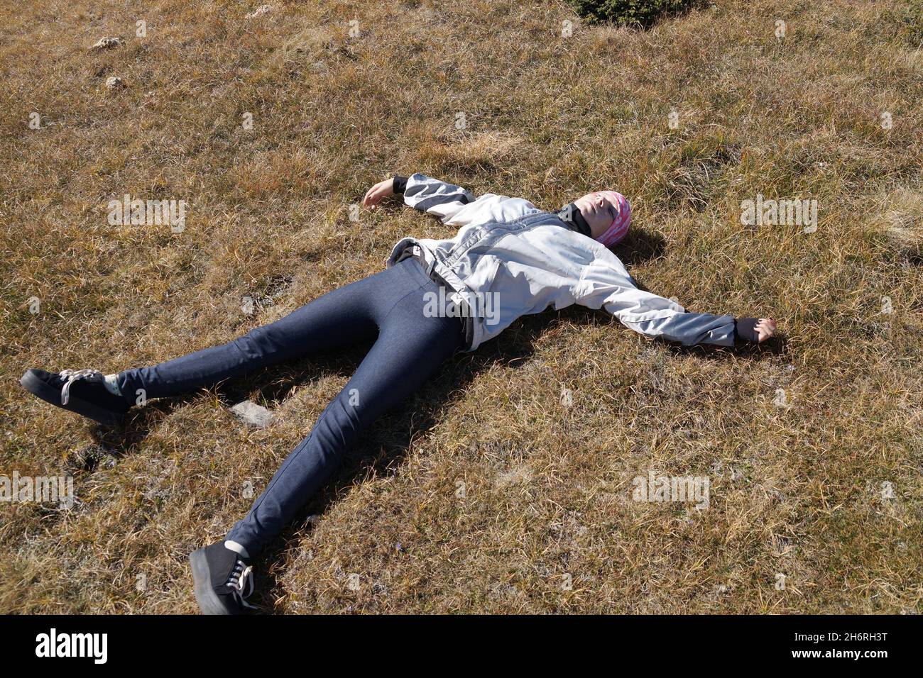 resting teenage girl lying on the ground with outstretched arms on a plateau in the mountains, halt Stock Photo