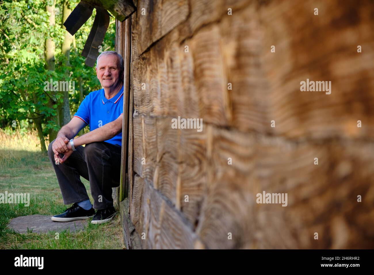 an elderly man sits on the threshold of a wooden hut looking into the distance Stock Photo