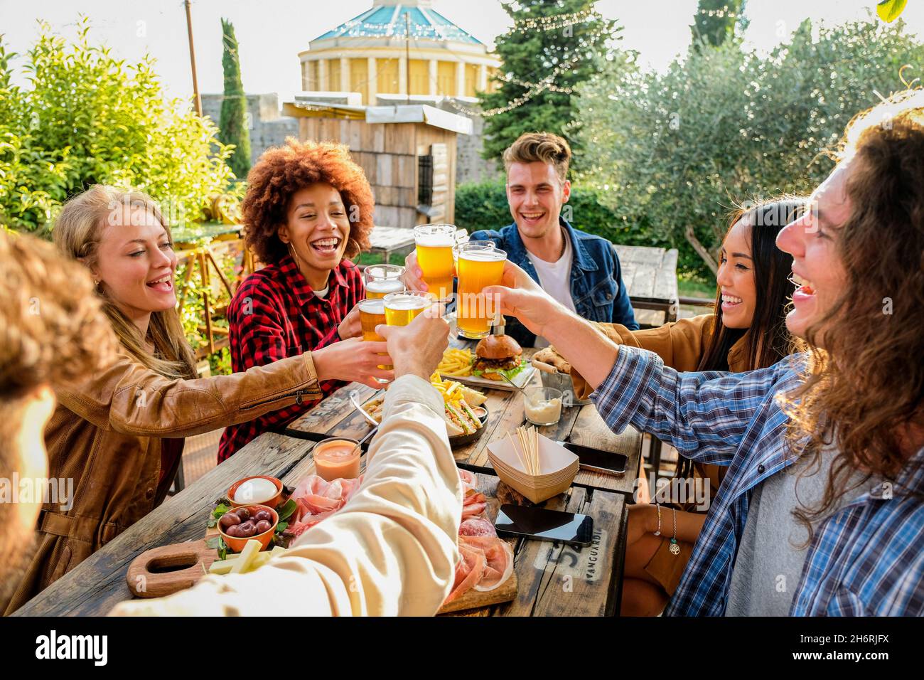 Group of multiethnic happy friends living healthy lifestyle and relaxing while drinking beer at outdoor pub restaurant - Young people enjoying drinks Stock Photo