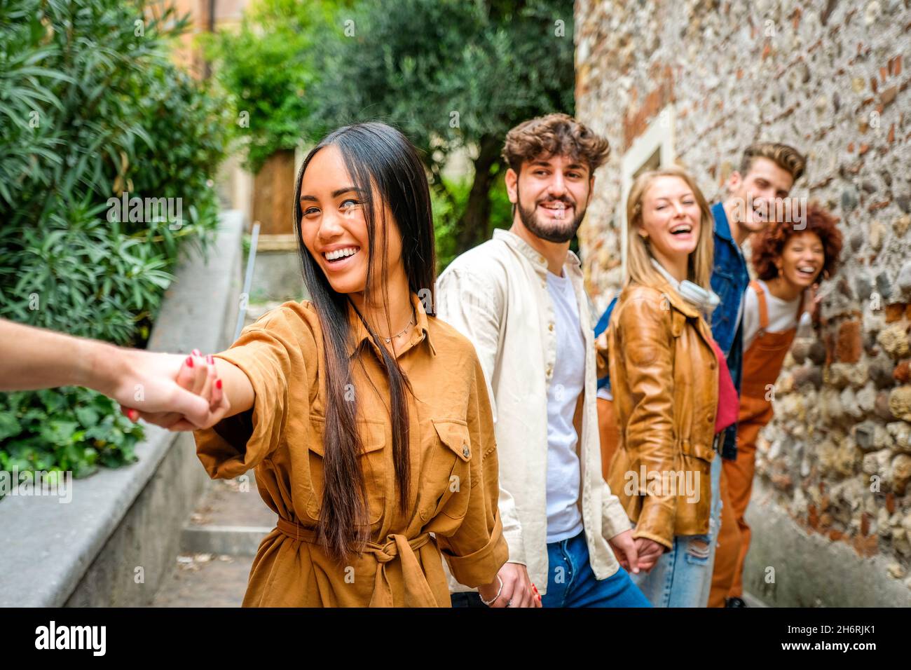Multiethnic group of teenagers walking in the city holding hands - Young people smiling and running down an alley stairs Stock Photo