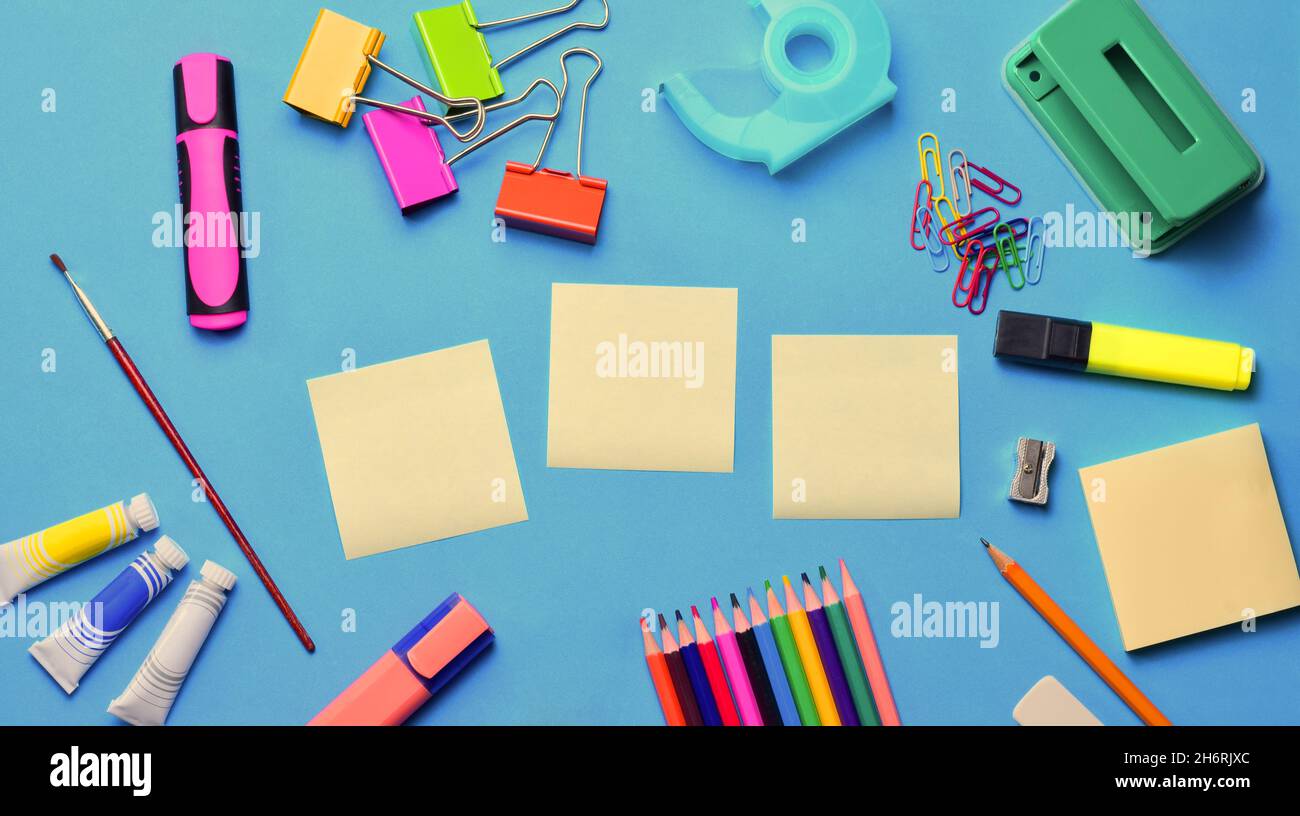 Top view of blank sticky notes and various school supplies on a blue surface - copy space Stock Photo