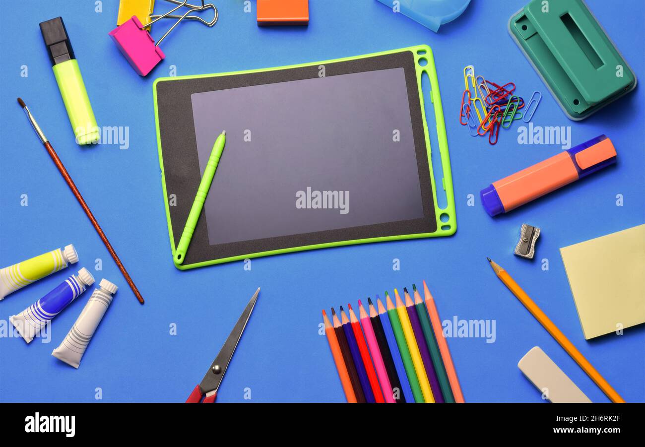 Top view of a tablet and various school supplies on a blue surface - copy space Stock Photo