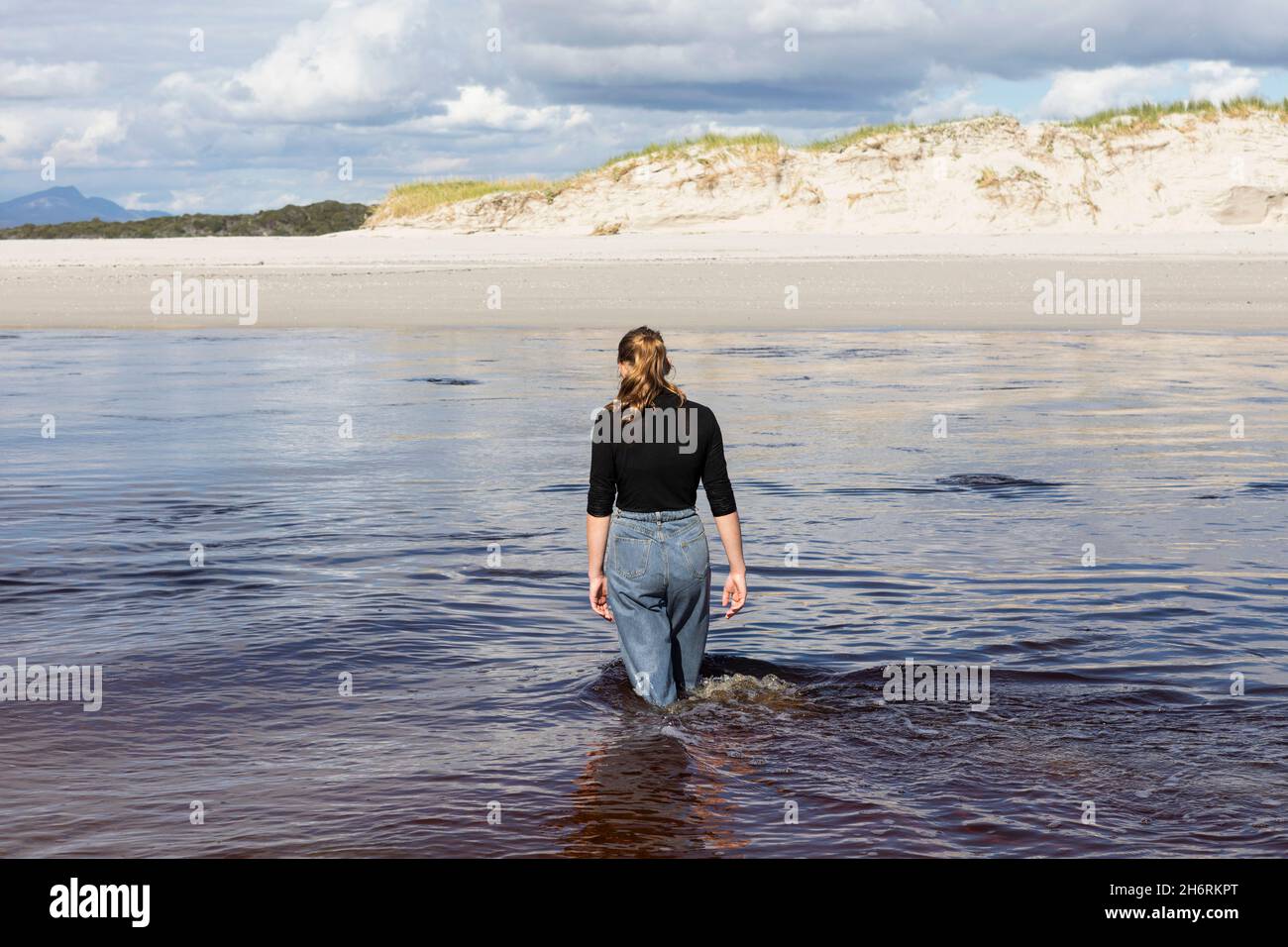 A teenage girl wading through a water channel on a wide sandy beach. Stock Photo