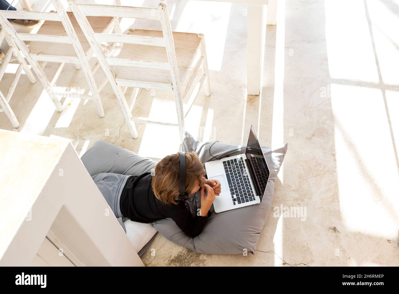 Eight year old boy lying on the floor on cushions using a laptop Stock Photo