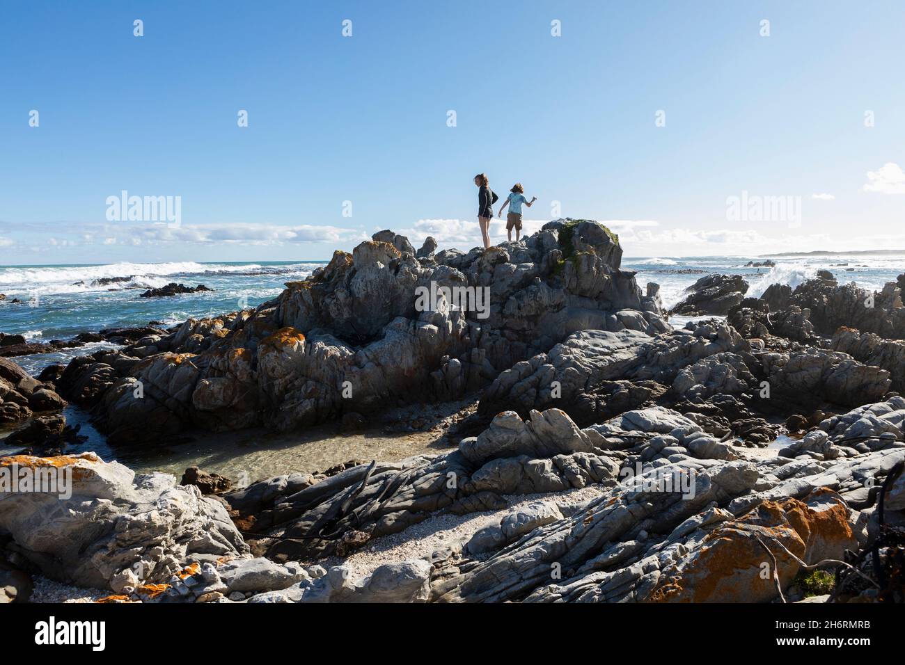 Two children, a teenage girl and eight year old boy exploring the jagged rocks and rockpools on a beach. Stock Photo