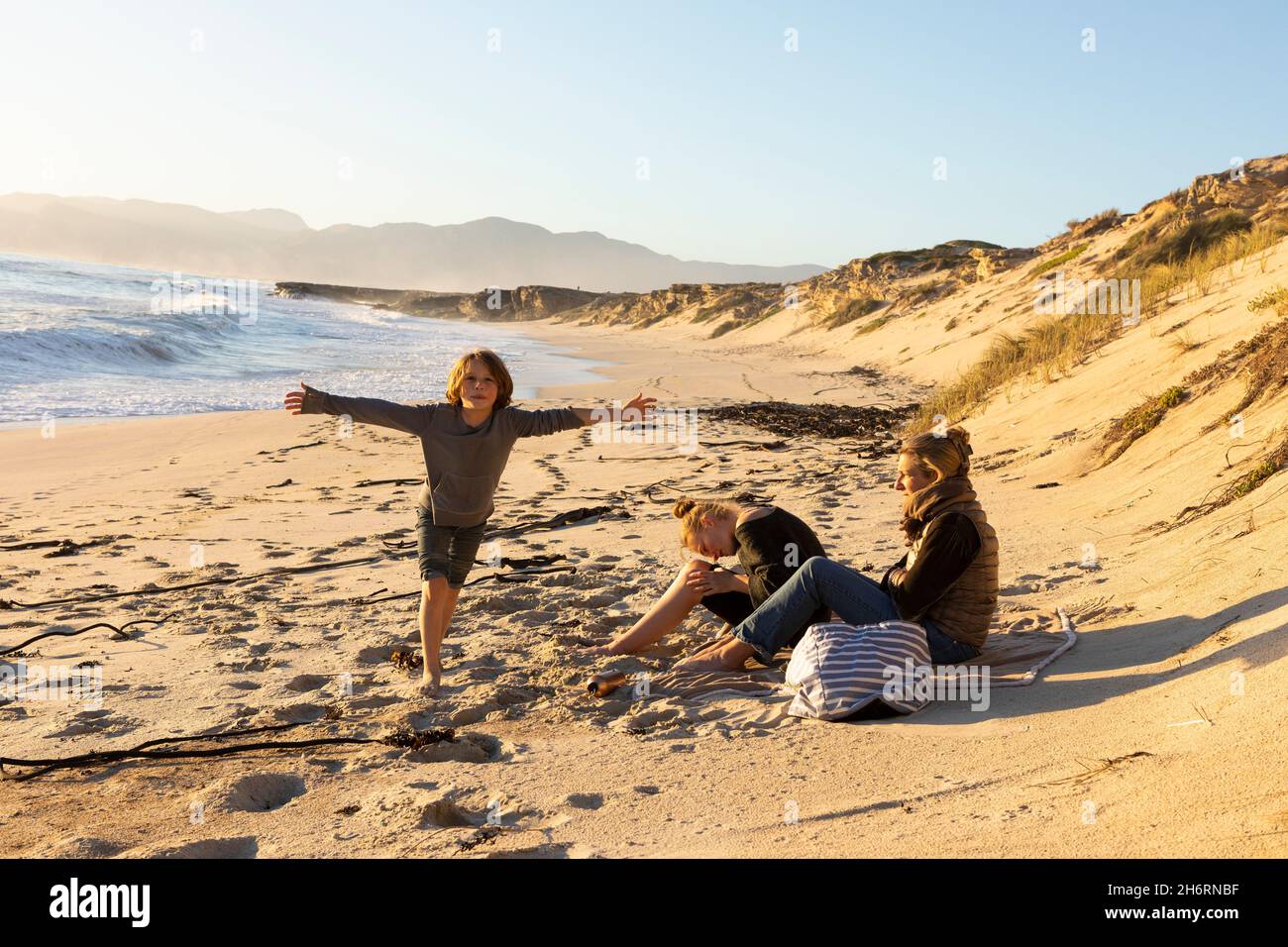 Family, mother daughter and son seated on a sandy beach looking out to sea. Stock Photo