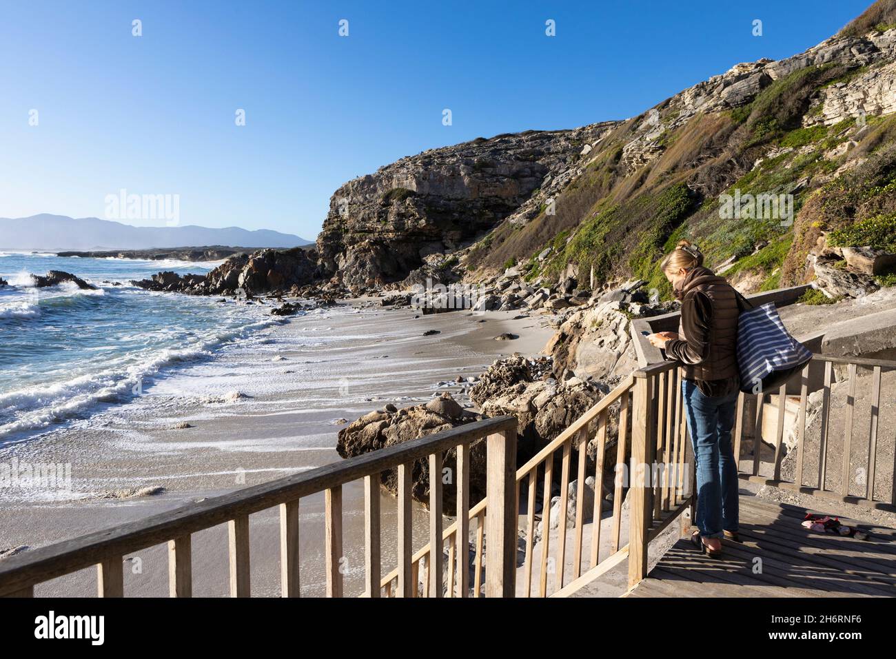 A mature woman standing on a walkway overlooking a sandy beach Stock Photo