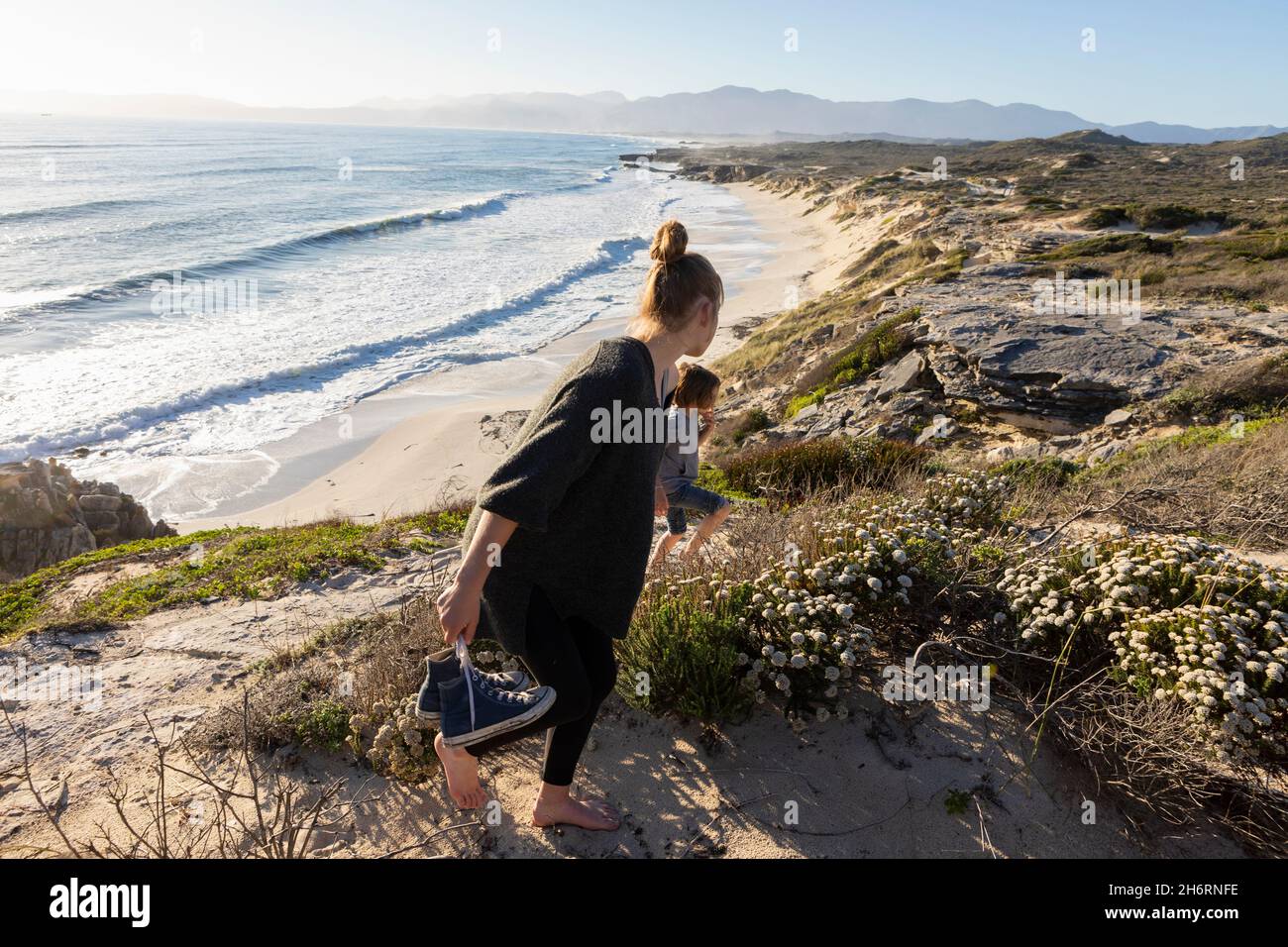 A teenage girl and her brother running down a path towards a sandy beach Stock Photo