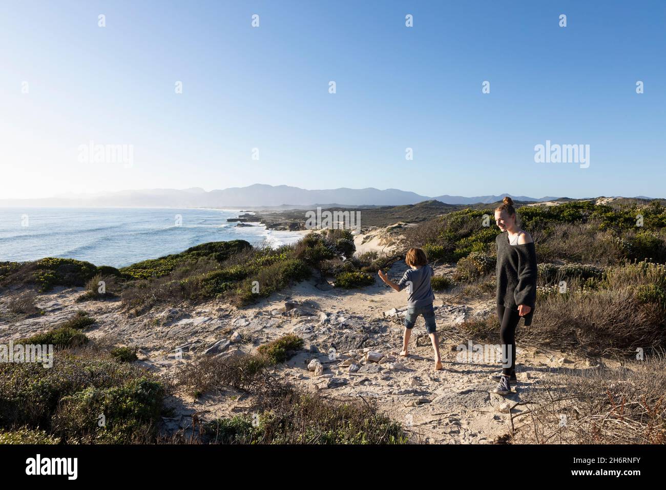 Two children, a teenager and her brother on a sandy path above a beach. Stock Photo