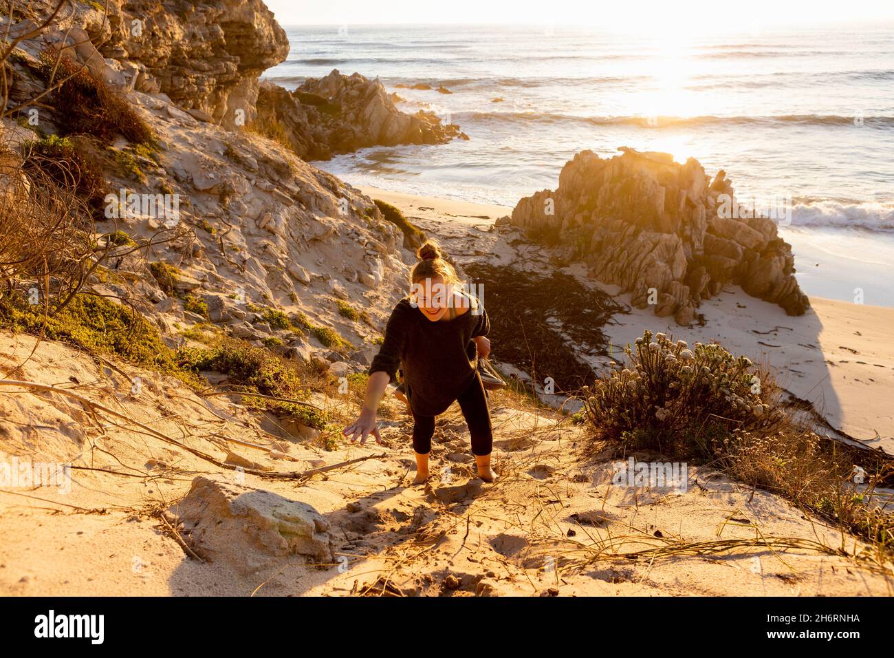 Teenage girl climbing up a very steep sandy slope above a beach Stock Photo