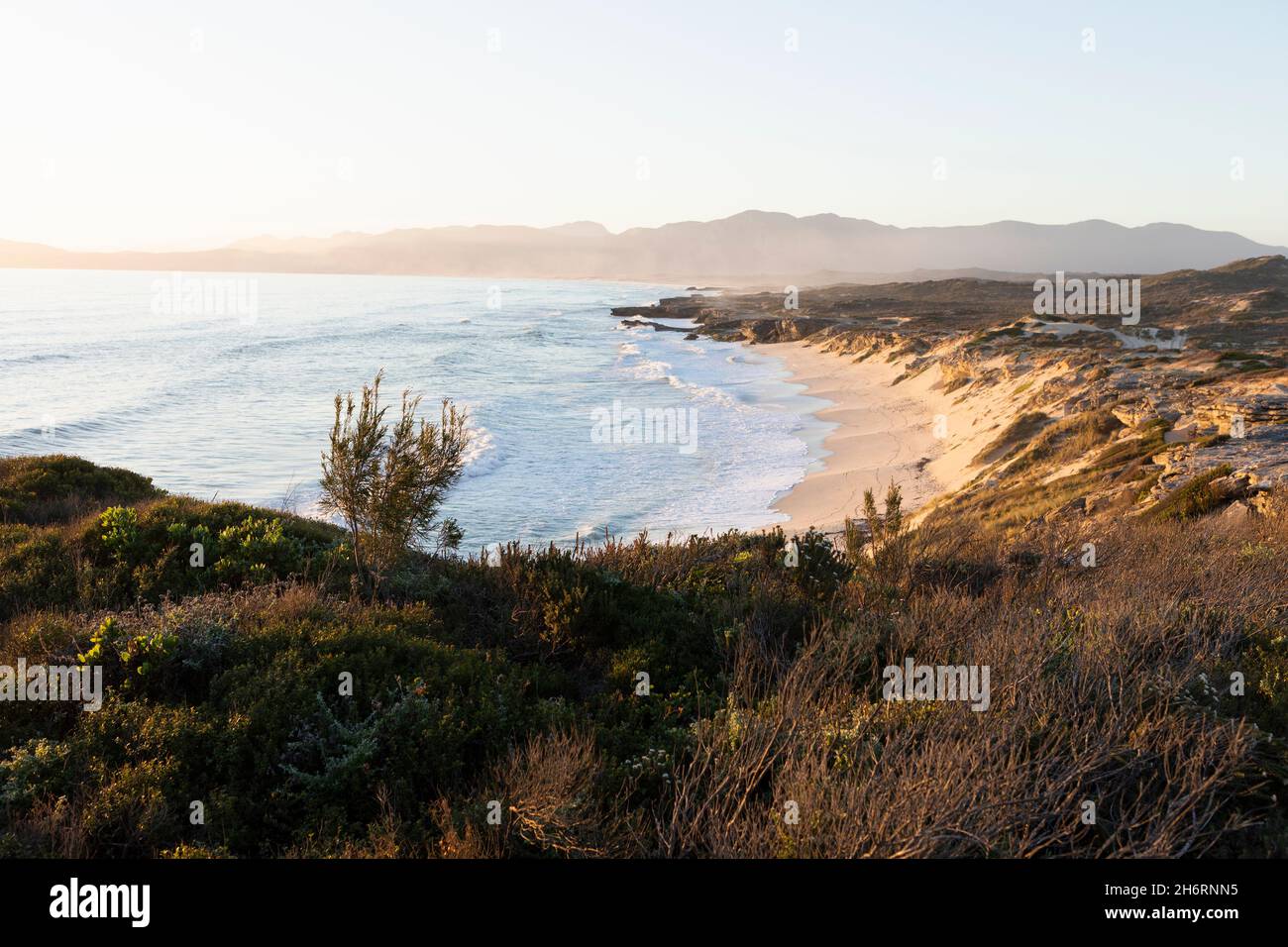 View from the cliffs over the sandy beach and waves breaking on shore. Stock Photo