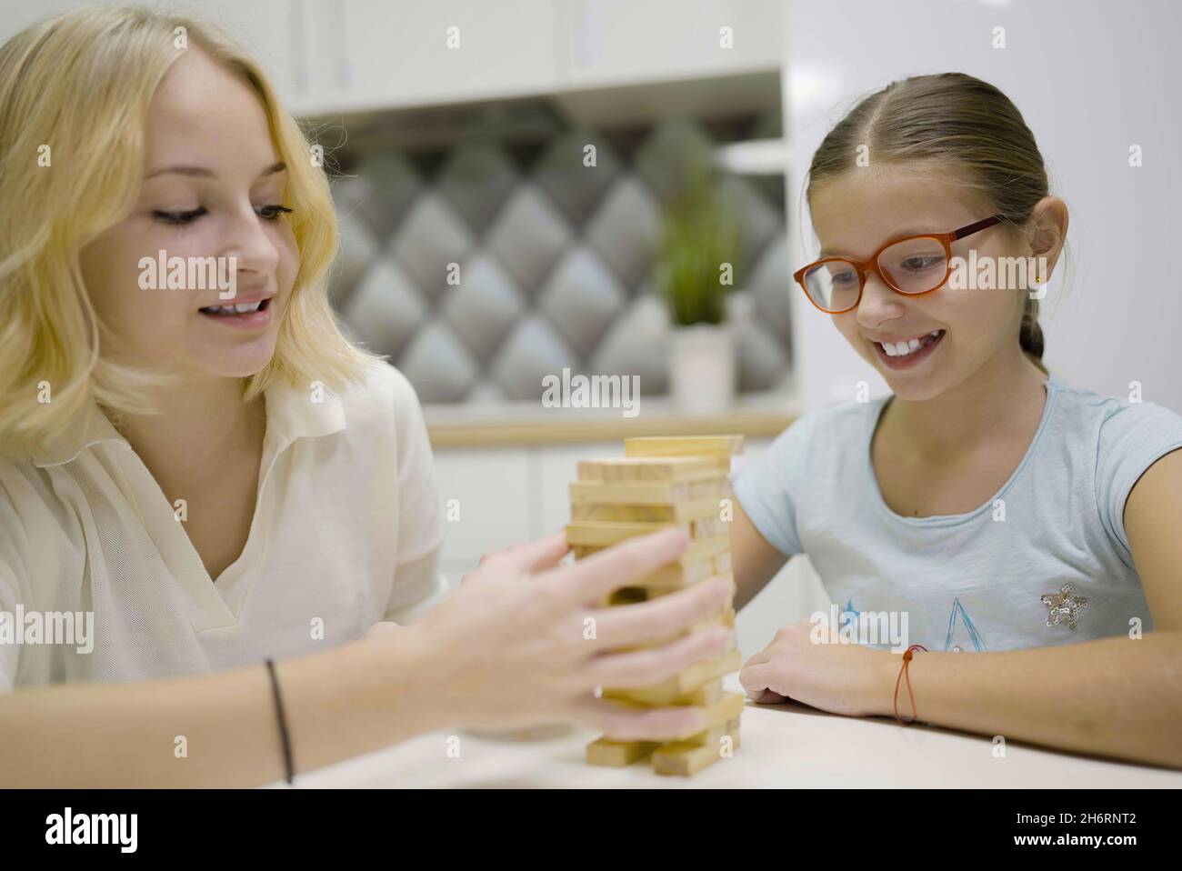 two girls have fun playing Jenga together - board game to remove wooden blocks and kids leisure concept. Stock Photo