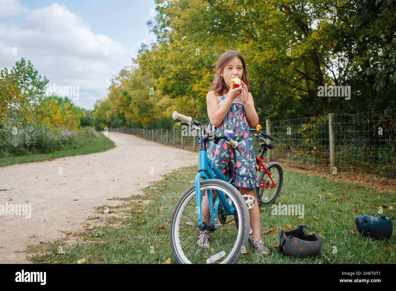 A little girl on bike takes break to eat apple in summer Stock Photo