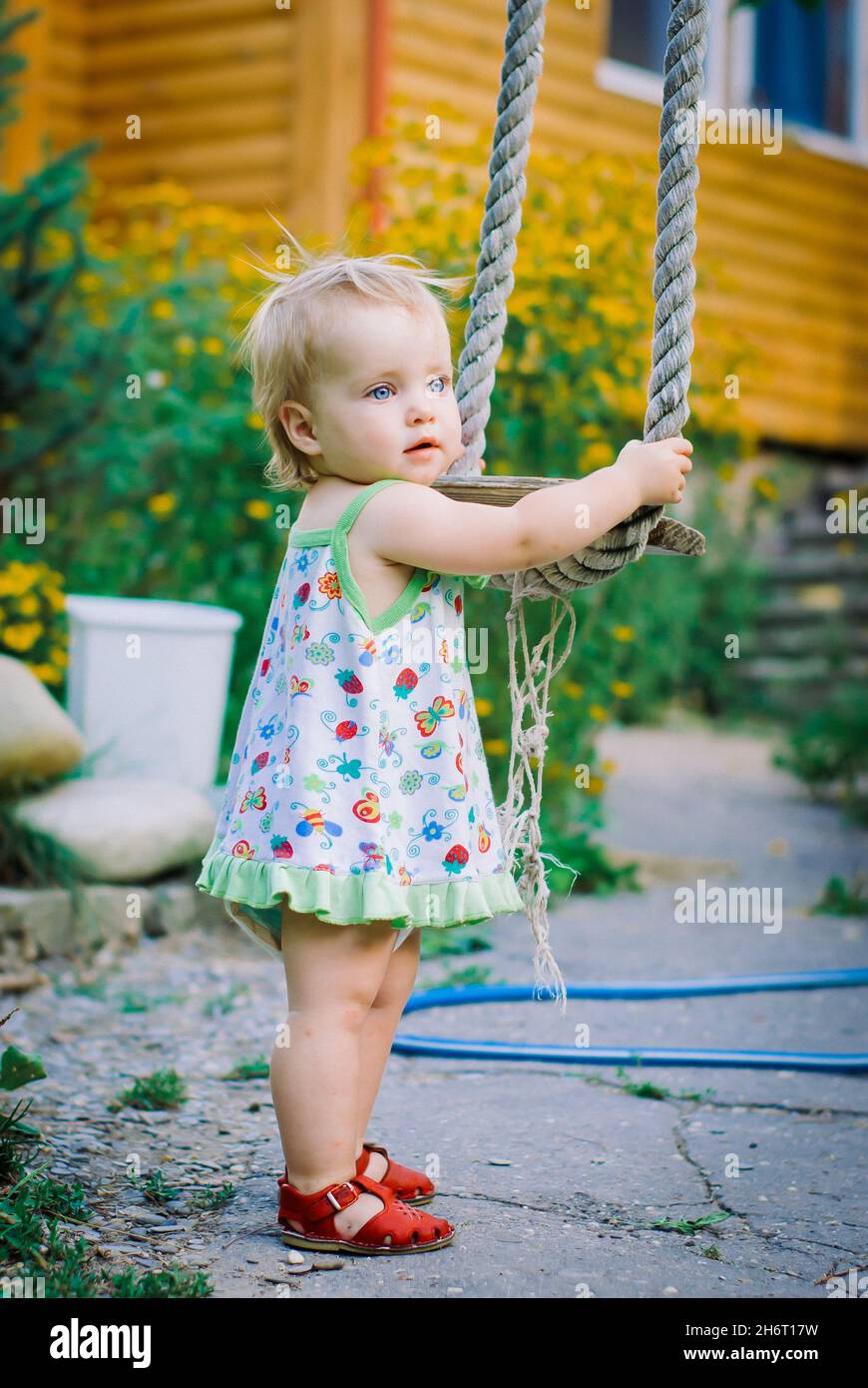 Cute baby girl 3 4 year old in the garden plays a rustic swing