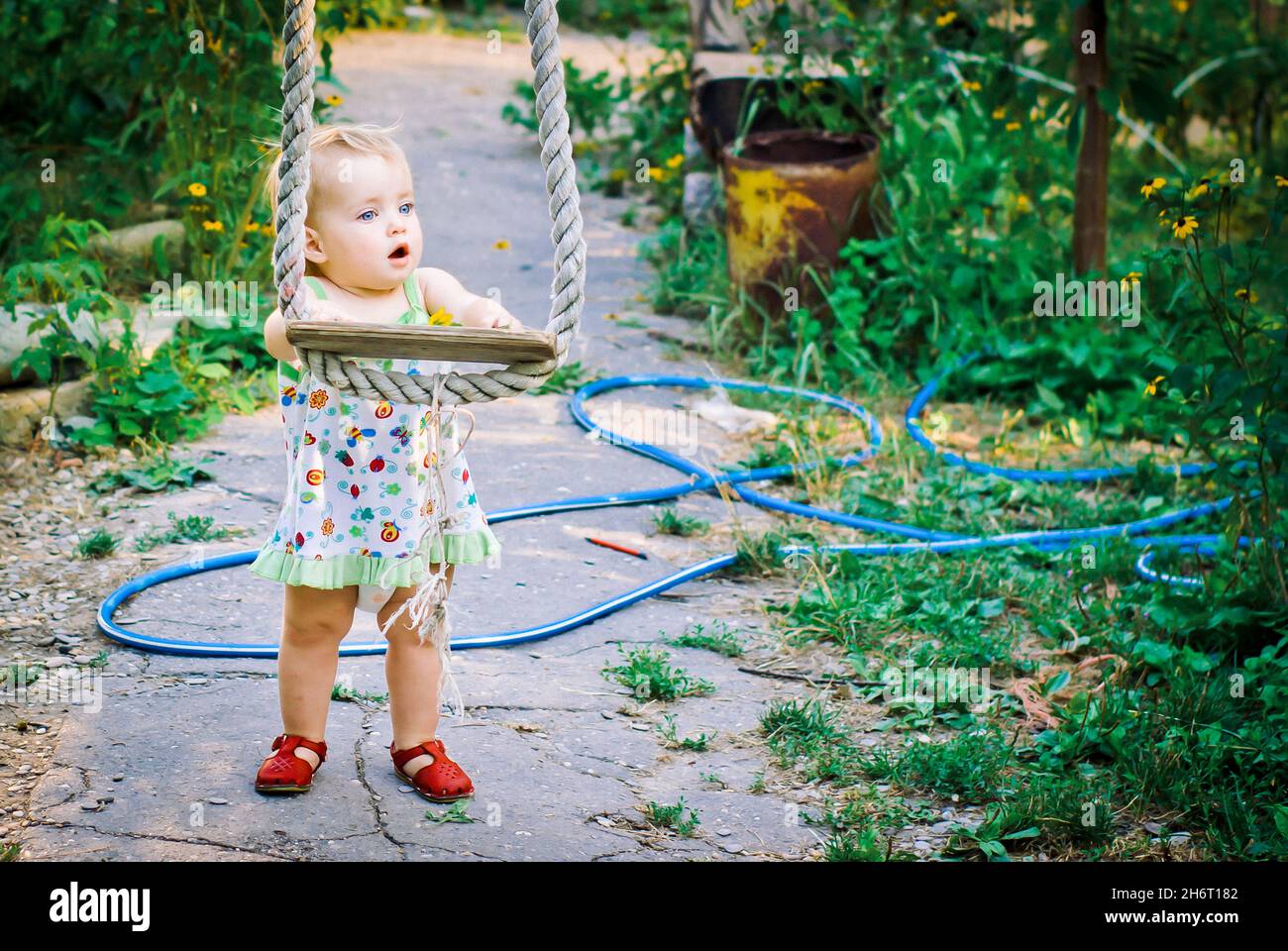 Cute baby girl 34 year old in the garden plays a rustic swing Stock