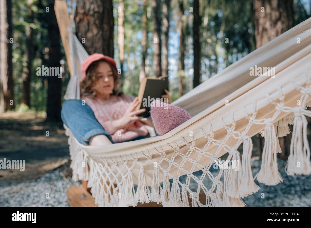 Woman in hammock reading book in forest, soft focus. Stock Photo
