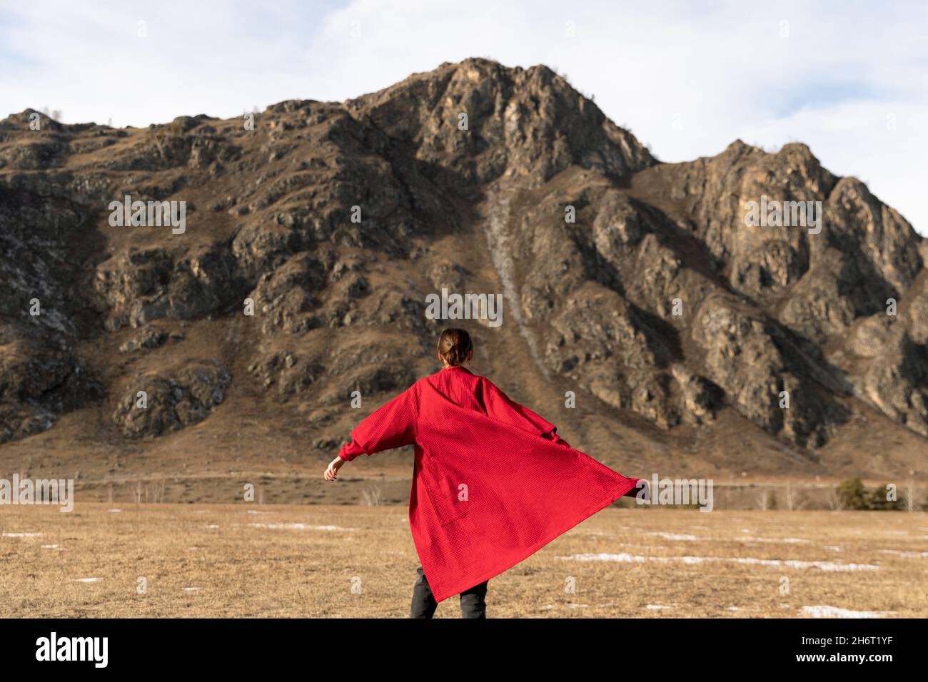Woman from back in a red bathrobe runs next to the mountain Stock Photo