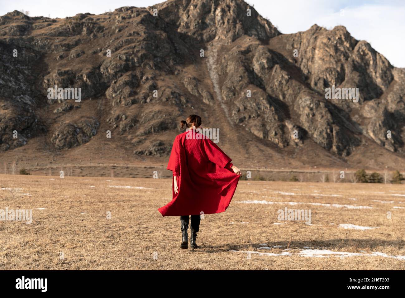 Woman from the back in a red coat runs next to the mountain Stock Photo