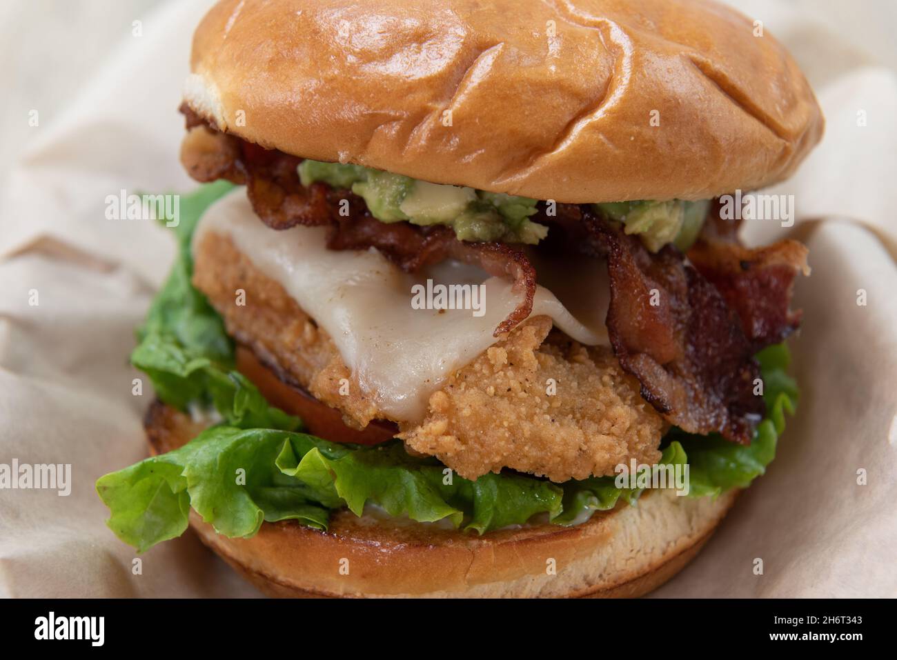Close up texture of a fried chicken club sandwich with melted cheese, bacon, lettuce, and tomato on a toasted bun. Stock Photo