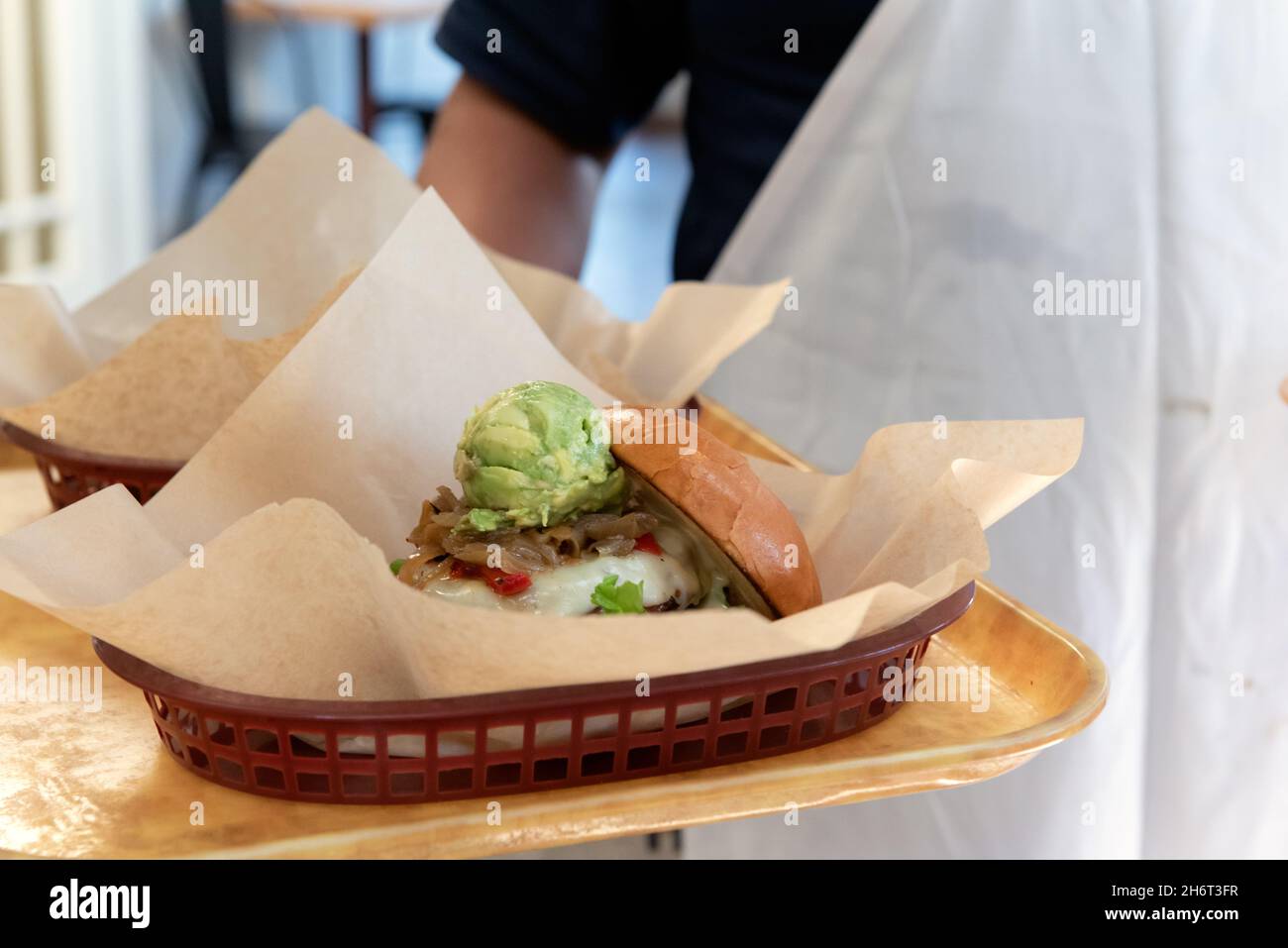 Waiter bringing the restaurant burgers and sandwiches on a tray wearing an apron. Stock Photo