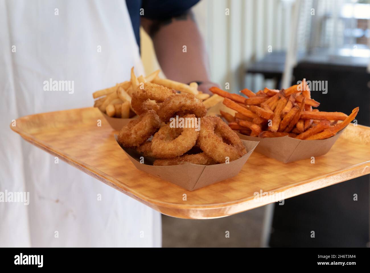 Waiter bringing the restaurant onion rings and french fries on a tray wearing an apron. Stock Photo