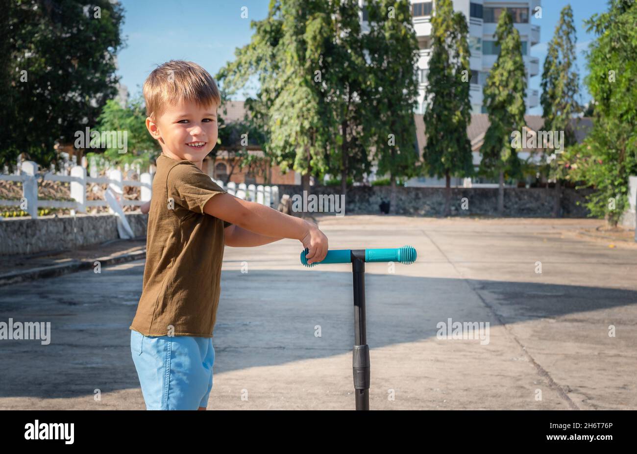 Portrait of a child with a scooter outside. The boy smiles and holds a scooter. Stock Photo