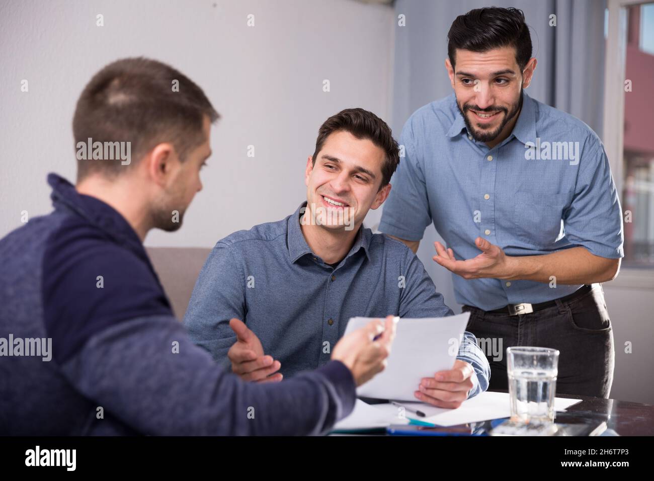 Three smiling men discussing papers at desk Stock Photo