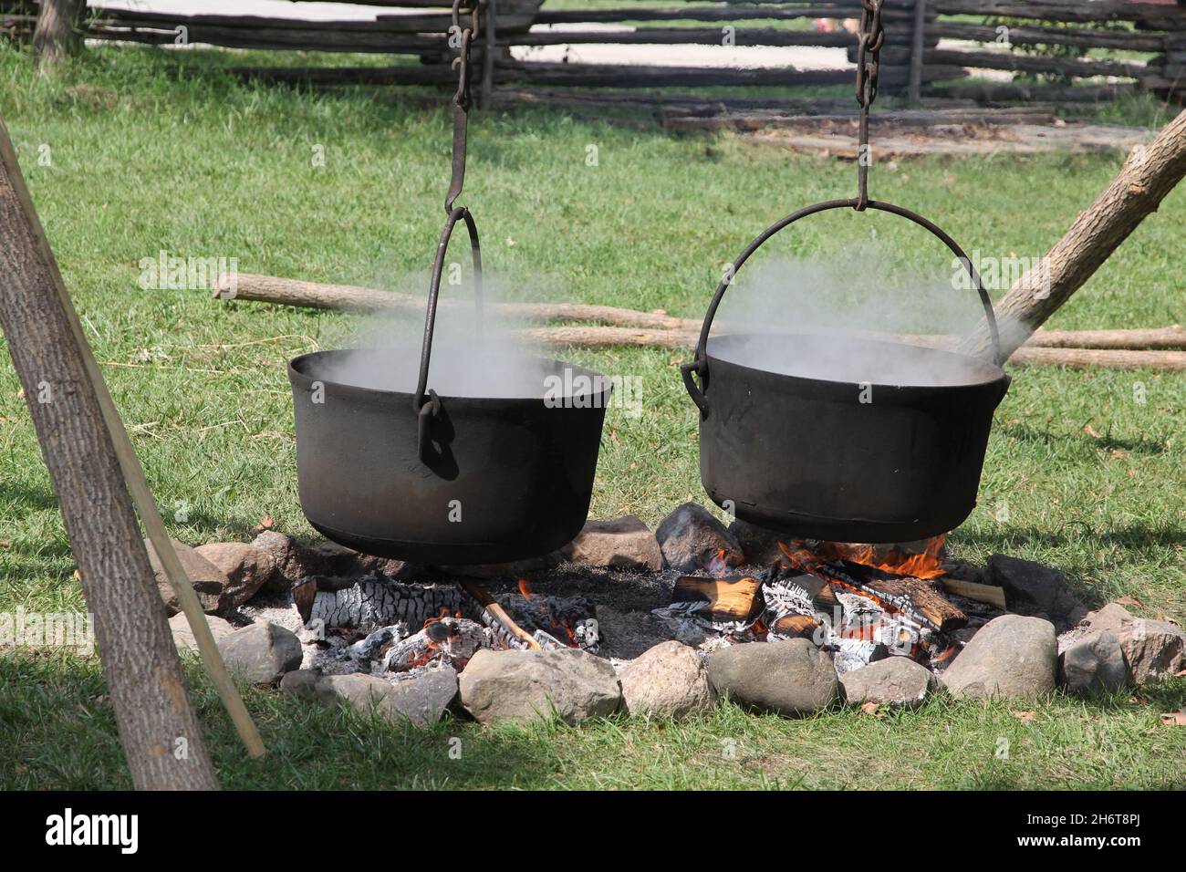 Two large cast iron cauldrons steaming over cooking fire outdoors Stock
