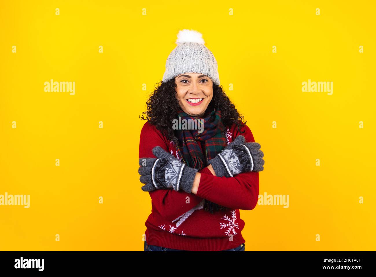 hispanic adult woman with frozen face and cold in winter sweater and warming up holding arms crossed on yellow background in Mexico Latin America Stock Photo
