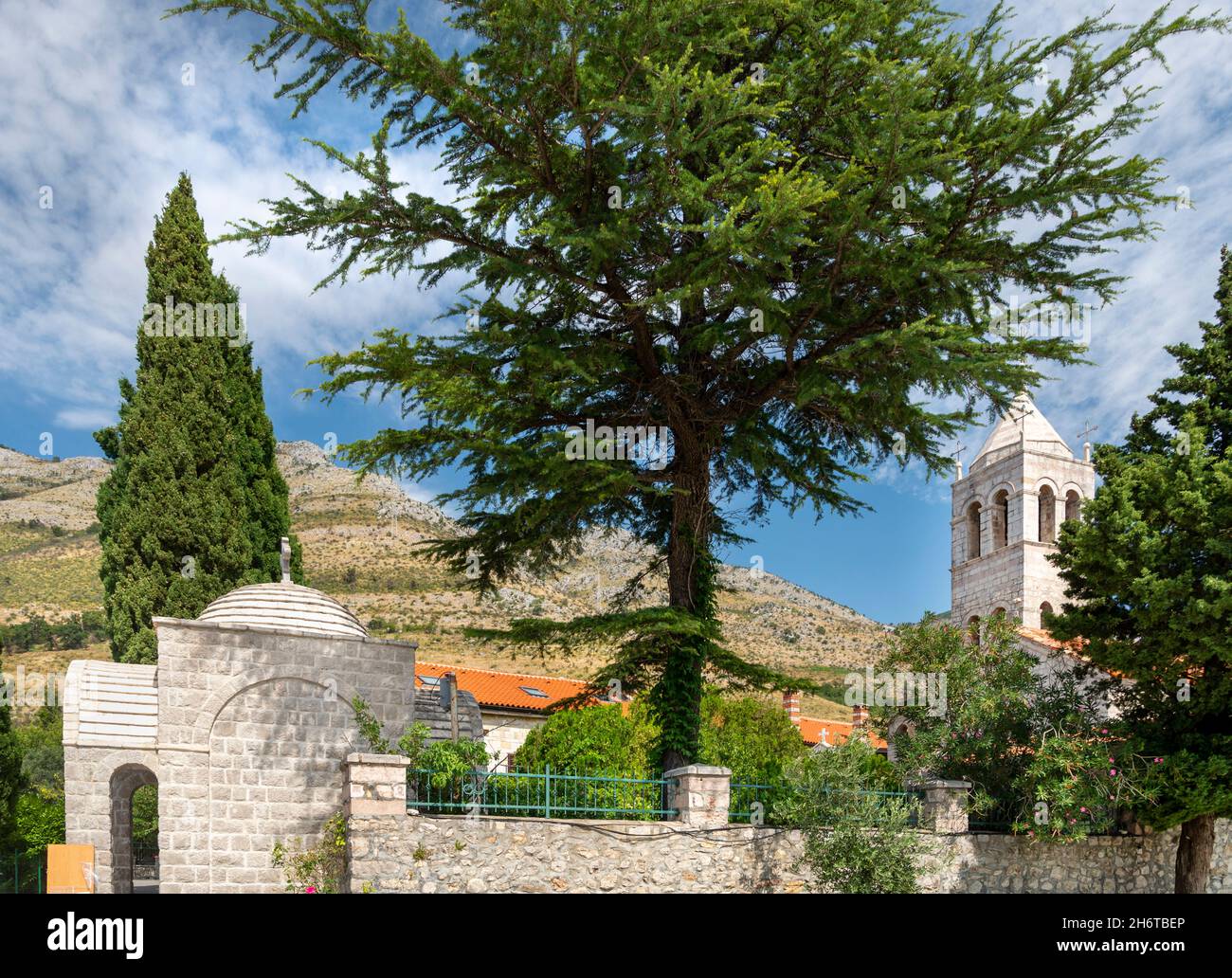 Small Serbian Orthodox style Church,surrounded by tall green trees inSeptember near Skadar Lake,in the mountains,with blue sky and wispy white clouds. Stock Photo